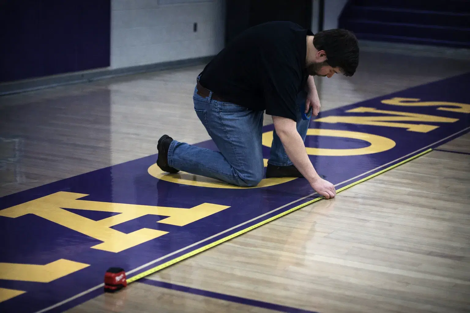 Luxedo technician measuring and taping a basketball court floor before projection mapping installation